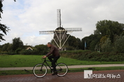 암스테르담 강 옆 풍차 앞을 자전거로 지나가는 시민