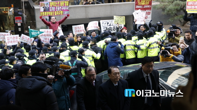 특검사무실이 입주해 있는 빌딩으로 들어서는 김기춘 전 실장 뒤로 많은 시민들이 피켓을 들고 "김기춘을 구속하라"고 외치고 있다.