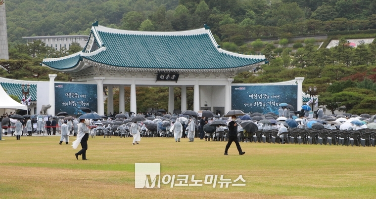 현충문 앞에서 열릴 추념식에 참석한 참석자들. 우천으로 인해 우비와 우산을 쓰고 있다.