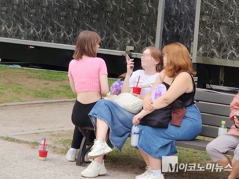 아직은 여유로워 보이는 외국인 팬들이 벤치에 앉아서 BTS 공연 장면을 보고 있다. 