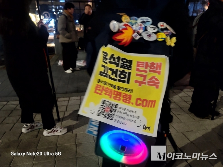 한 참가자의 백백에 달려 있는 야광봉과 미니헌수막. 헌수막에는 "윤석열 탄핵, 김건희 구속',' '윤석열 탄핵을 발의하라! 탄핵명령 com이라는 문구가 보인다.