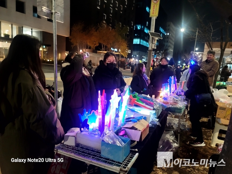 집회 인근에는 아이돌 콘서트장에서 볼 수 있을 법한 응원봉을 판매하는 판매대가 늘어서 있다.. 젊은 여성 여럿이 응원봉을 보면서 대화를 나누고 있다.
